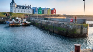 A harbor with a white building, colorful houses, and a boat. - Northstar - 4 Bed Luxury Apartment (Wick)