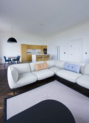 A modern living room with a sectional sofa, a dining table with chairs, and a kitchen area in the background. - Shoeburn (Isle of Lewis)
