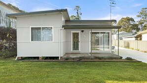A single-story house with a front porch, a sliding glass door, and a small front yard. - Wanderer by Experience Jervis Bay (Sanctuary Point)