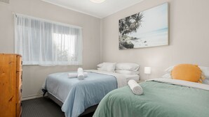 A hotel room with two beds, a wooden dresser, a window with sheer curtains, and a beach-themed painting on the wall. - Wanderer by Experience Jervis Bay (Sanctuary Point)