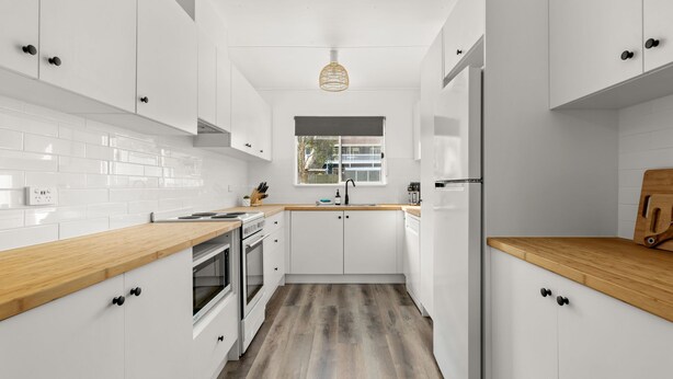 A modern kitchen with white cabinetry, wooden countertops, a built-in oven, and a window above the sink. - Wanderer by Experience Jervis Bay (Sanctuary Point)