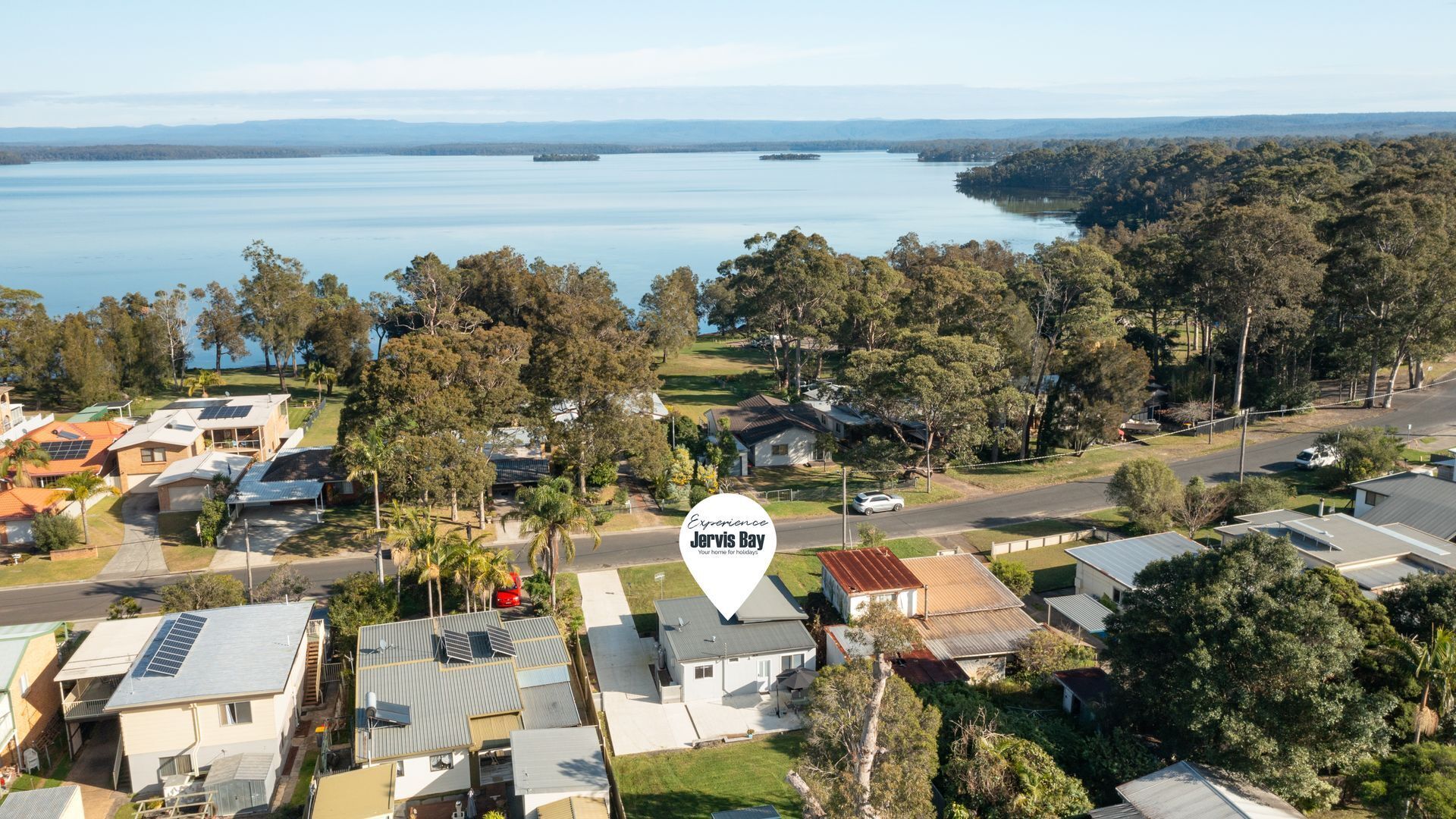 An aerial view of a residential area with houses, solar panels, and a large body of water in the background.