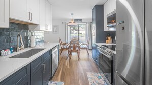 A modern kitchen with a stainless steel refrigerator, a built-in oven, and a large sink. There is a dining area with a wooden table and chairs. - Seascape Villa 92F *Beach access and multiple pools! (Miramar Beach)