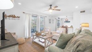 A spacious living room with a large window, a ceiling fan, and a cozy green sofa. - Seascape Villa 92F *Beach access and multiple pools! (Miramar Beach)