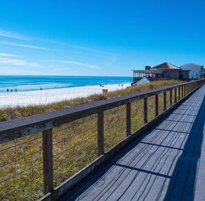 A wooden boardwalk leading to a beach with a restaurant named "Whale's Tail" in the background.