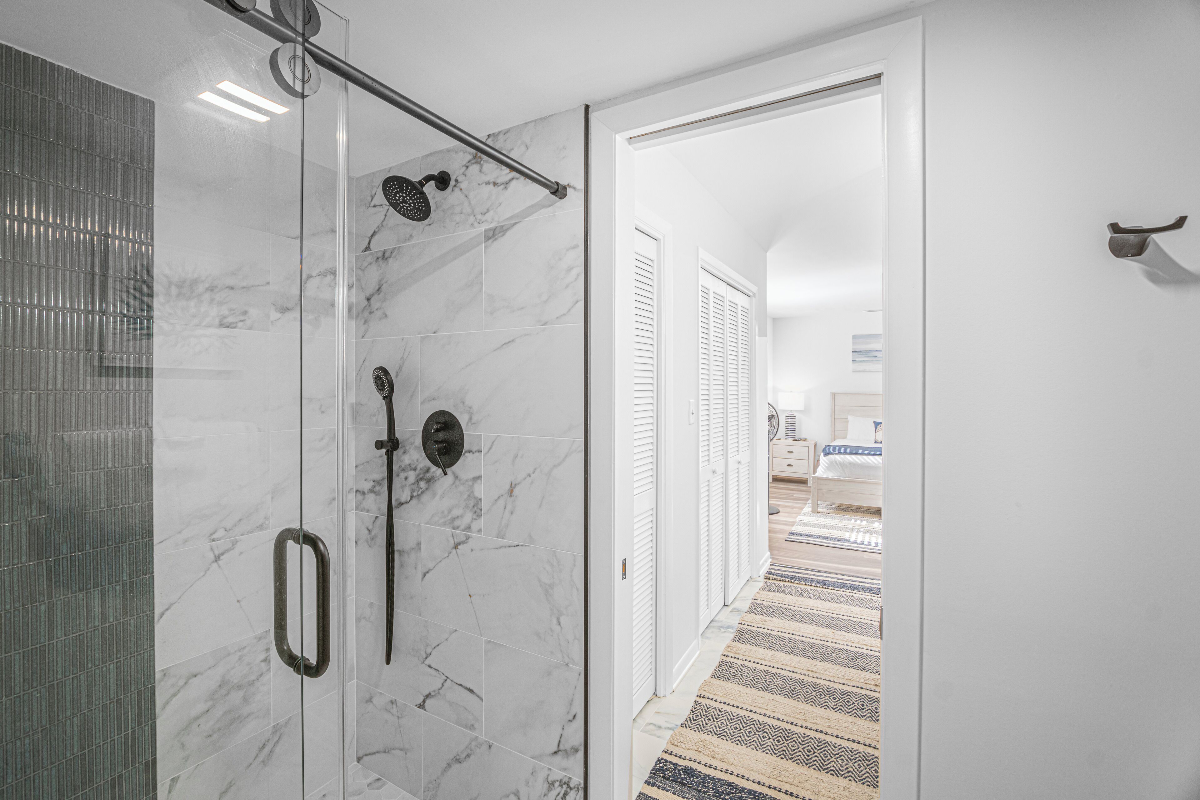 A modern bathroom with a glass shower enclosure, marble tiles, and a visible showerhead.