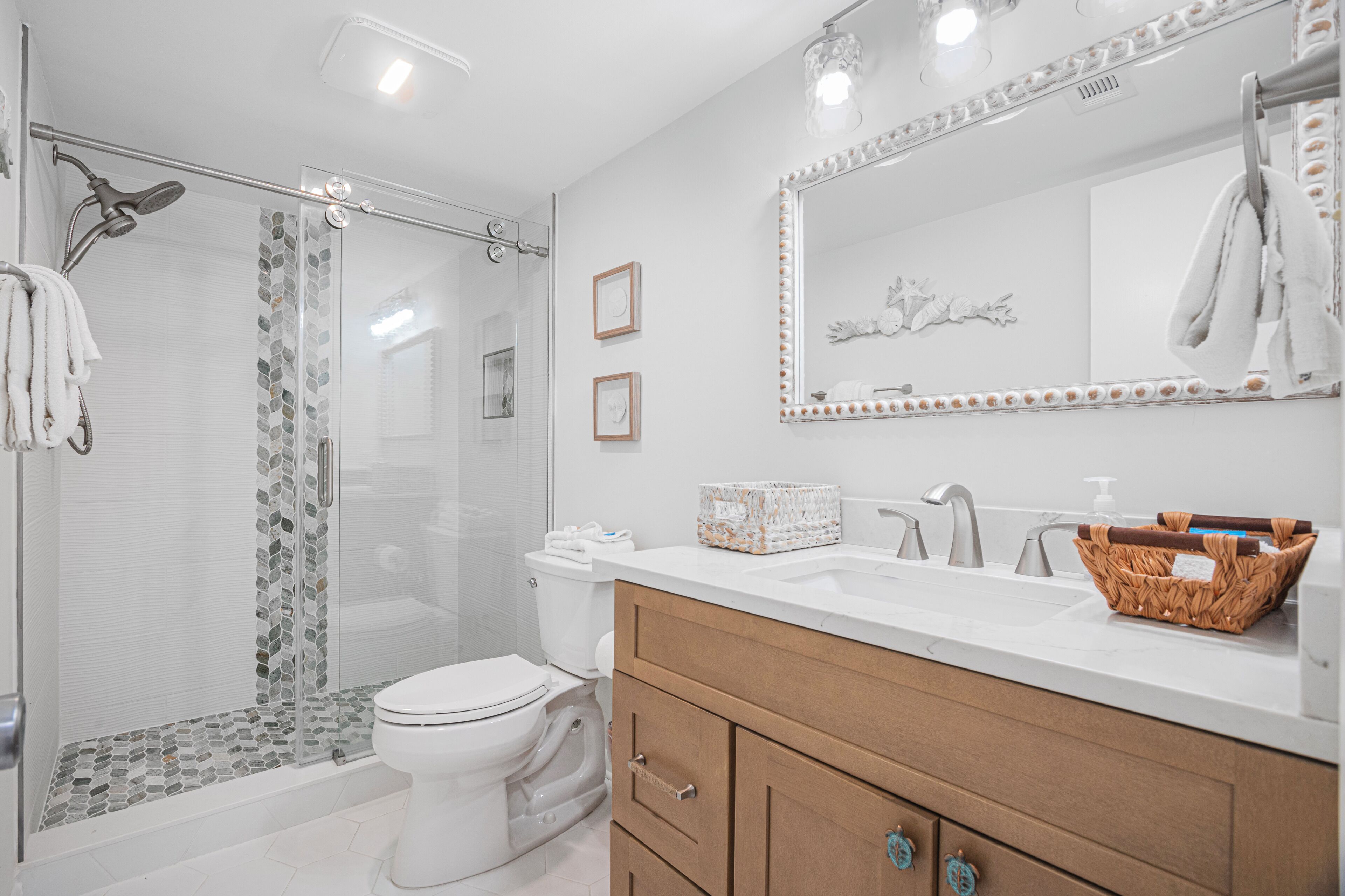 A modern bathroom with a glass shower enclosure, a white toilet, a wooden vanity with drawers, and a large mirror with a decorative frame.