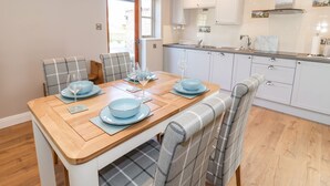 Une cuisine moderne avec des meubles blancs, une table à manger en bois dressée avec des assiettes bleues et des verres à vin, et une horloge au mur.