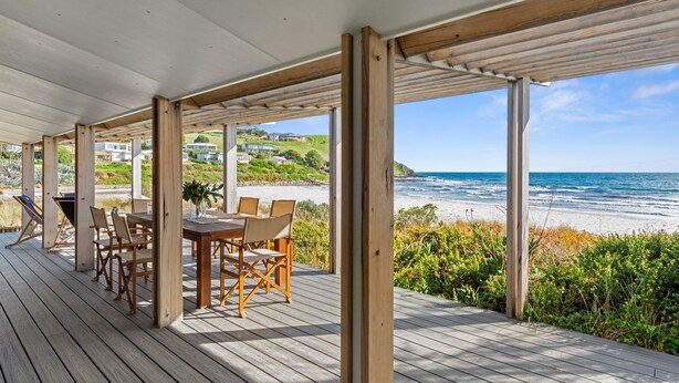 A wooden deck with a table and chairs, overlooking a beach and ocean. - Myponga Dunes - 1 Hewett Crescent, Myponga Beach (Myponga Beach)
