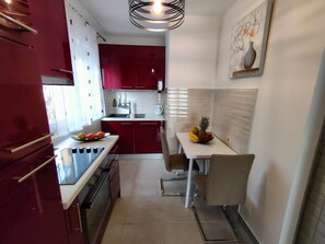 A compact kitchen with red cabinets, a white countertop, and a dining area with a table and chairs. - A1 Beachfront apt With big Terrace and sea View (Podstrana)