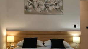 A hotel room with a wooden headboard, two black pillows, a bed with white linens, and a painting of flowers on the wall. - A5 Beachfront apt With a Balcony and sea View (Podstrana)
