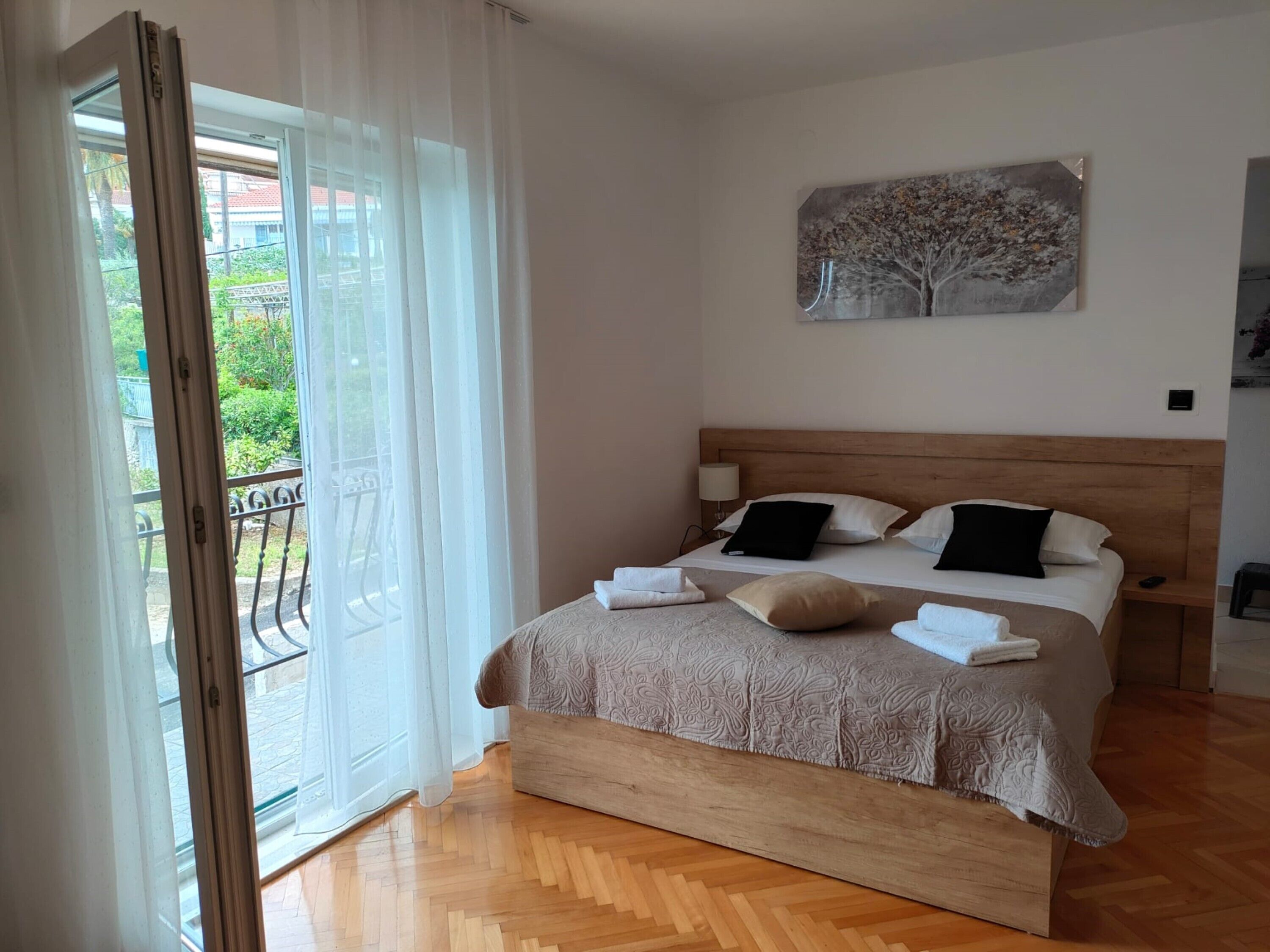 Une chambre avec un lit en bois, du linge de lit blanc et une vue sur le balcon.