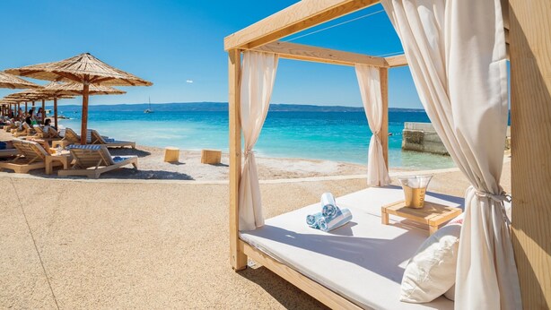 A beachside room with a wooden canopy bed, a view of the sea, and sun loungers with umbrellas. - A5 Beachfront apt With a Balcony and sea View (Podstrana)
