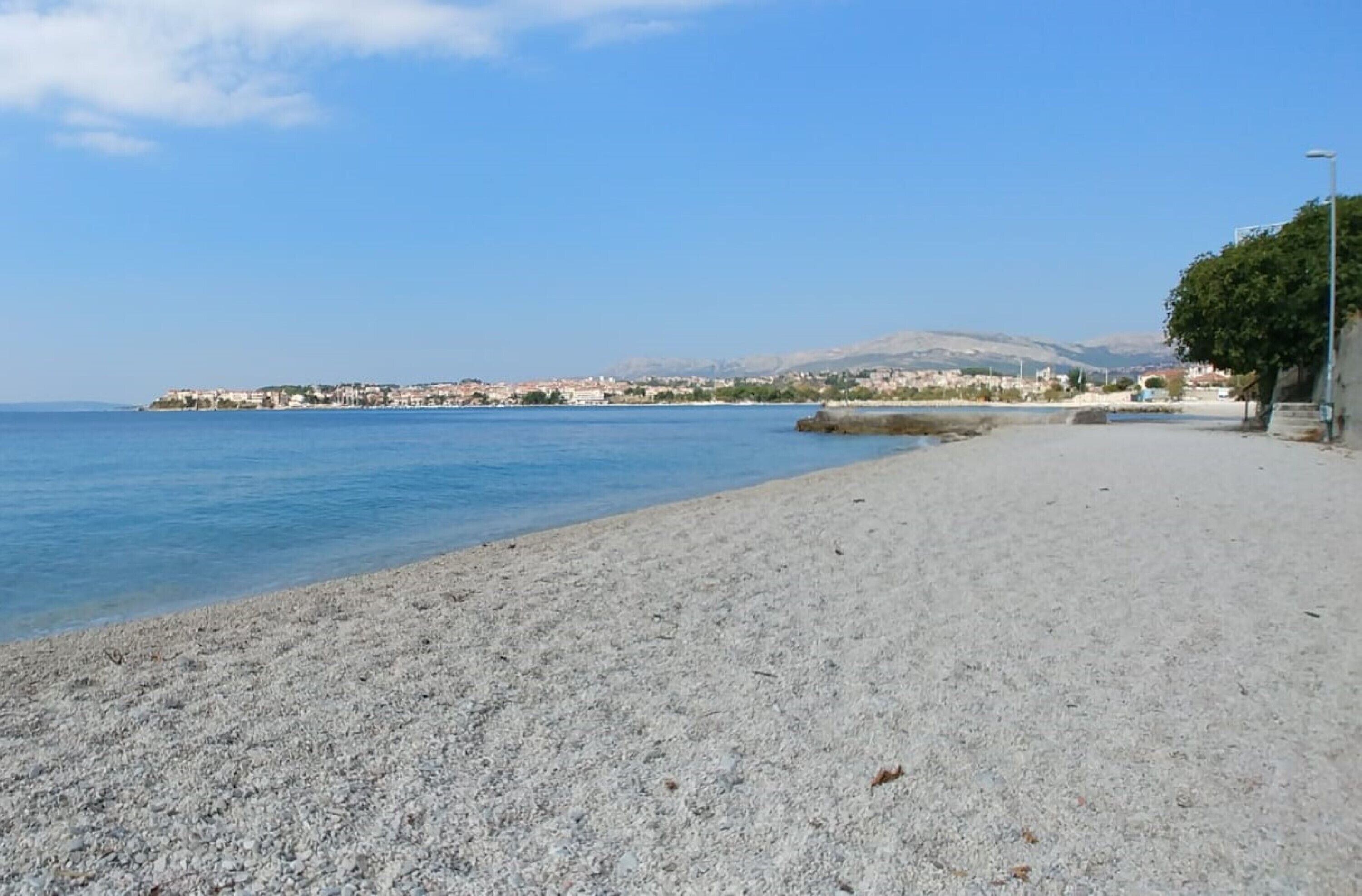 Una playa de guijarros con una vista despejada del mar y edificios lejanos.