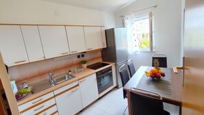 A modern kitchen with white cabinets, a stainless steel refrigerator, and a dining area with a table set for two. - A4 Beachfront apt With big Terrace and sea View (Podstrana)