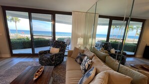 Un saló amb un finestral gran que dona a una platja, moblat amb un sofà, cadires i una taula de centre.
