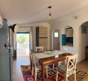 A dining area with a wooden table and chairs, a colorful rug, and a view of the outside.