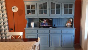 A kitchen with a TV on the counter, a white chair, and a patterned tablecloth. - Vacation home 180 mt from the sea, ideal with dogs (Tertenia)