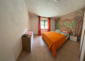 Ein Schlafzimmer mit einem Bett, einem Nachttisch, einem Fenster mit Vorhängen und einem Wandgemälde.