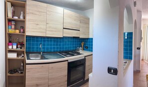 Eine kleine Küche mit Holzschränken, einer blauen Fliesenrückwand, einem Gasherd und einem Spülbecken.