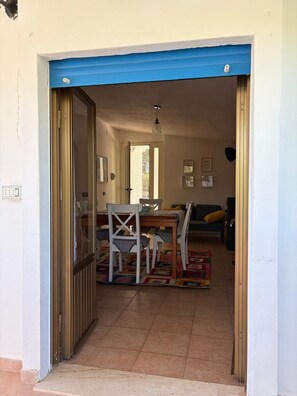 An open doorway leading to a dining area with a table and chairs, a patterned rug, and a view into a living room with a sofa and cushions. - Vacation home 180 mt from the sea, ideal with dogs (Tertenia)