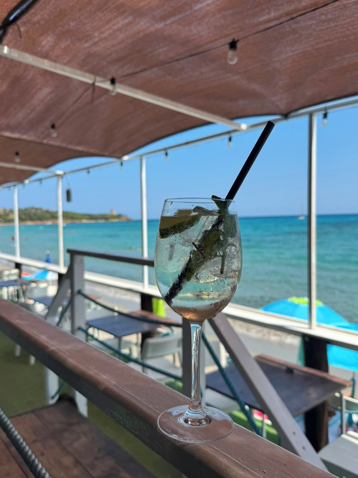 A glass of drink with a straw on a wooden bench, overlooking a body of water.