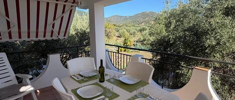 Una terraza con una mesa dispuesta para dos, sillas de plástico blancas y vistas al campo.