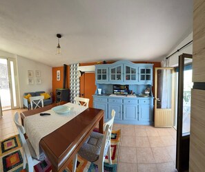 A compact kitchen with blue cabinets, a dining area with a wooden table, and a small TV. - Vacation home 180 mt from the sea, ideal with dogs (Tertenia)