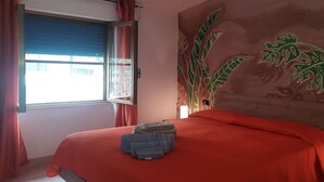 A bedroom with a bed, a window with curtains, and a wall with a leaf pattern. - Vacation home 180 mt from the sea, ideal with dogs (Tertenia)