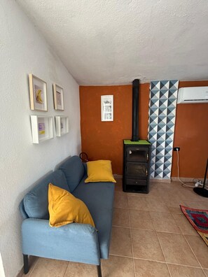 A living room with a blue sofa, yellow cushions, a fireplace, framed pictures on the wall, and a patterned wall. - Vacation home 180 mt from the sea, ideal with dogs (Tertenia)