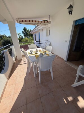 A covered outdoor dining area with a table set for four, surrounded by white chairs, a pergola overhead, and a view of a house in the background. - Vacation home 180 mt from the sea, ideal with dogs (Tertenia)