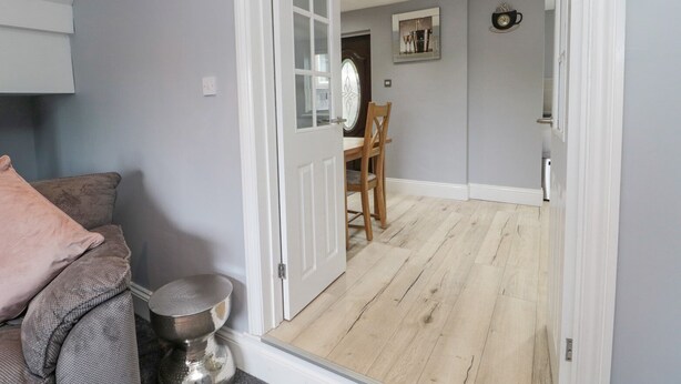 Una habitación con pared gris, piso de madera, puerta blanca, una mesa de comedor con sillas y una pequeña mesa redonda con base metálica.