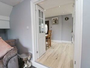 A room with a grey wall, a wooden floor, a white door, a dining table with chairs, and a small round table with a metal base. - 4 Tyne View (Hexham)