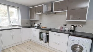 Una cocina moderna con armarios blancos, horno empotrado, lavadora y ventana con persianas.