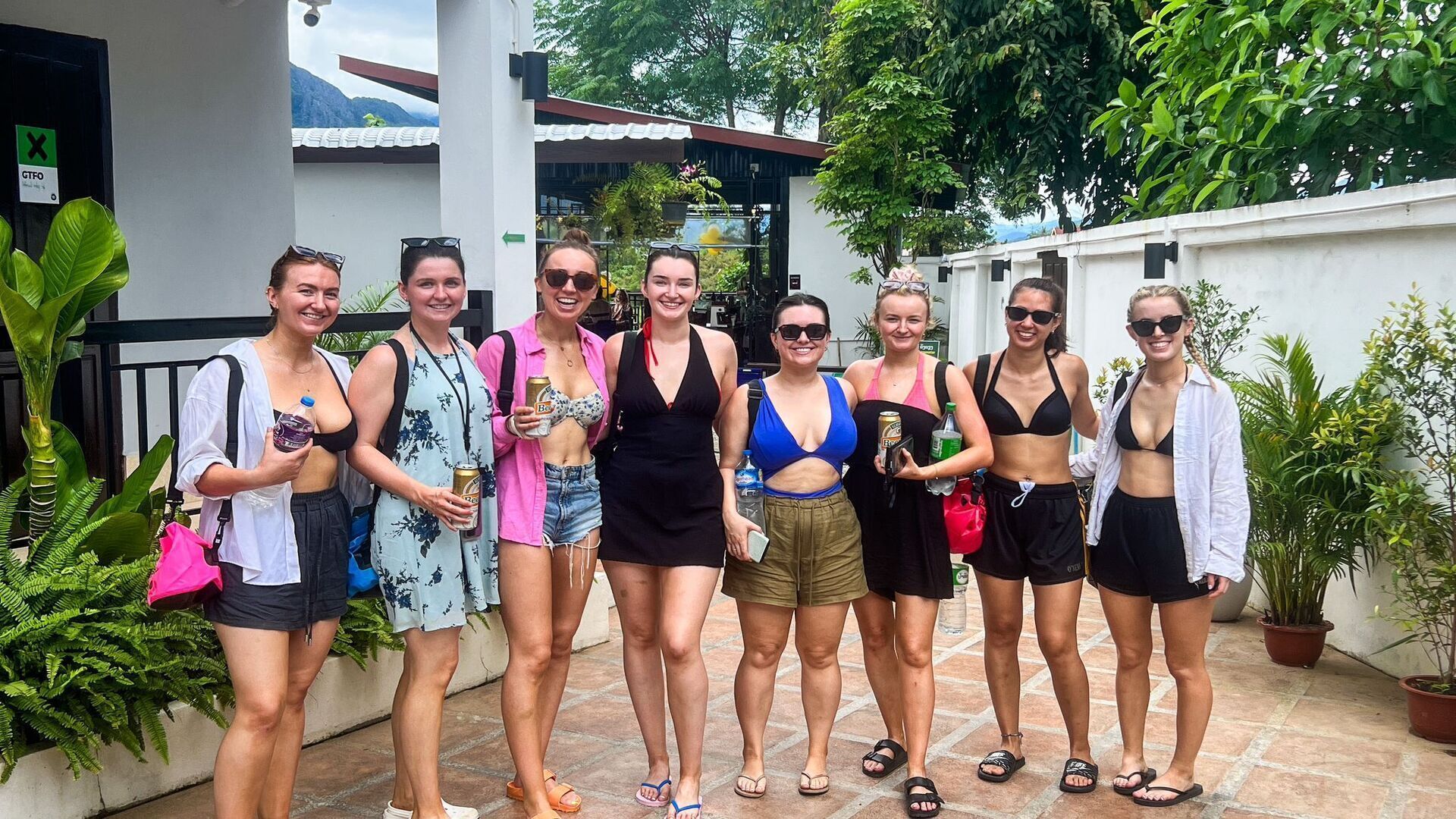 Un grupo de personas de pie al aire libre en un patio con plantas en macetas y un edificio al fondo.