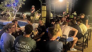 An outdoor gathering with people seated around tables, a stage with a performer, and a decorative tree with lights. - Mad Monkey  Vang Vieng (Vang Vieng)