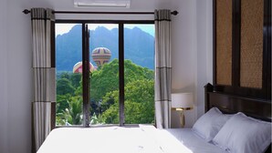 A hotel room with a large bed, a nightstand with a lamp, and a view of hot air balloons over a mountainous landscape. - Mad Monkey  Vang Vieng (Vang Vieng)
