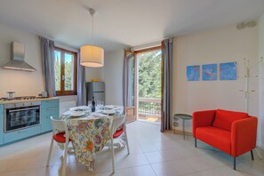 Un comedor con una mesa dispuesta para dos personas, un sofá rojo y un balcón con cortinas.