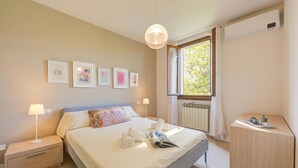 Habitación de hotel con cama, lámparas de noche, mesita de noche, ventana con vistas y obras de arte en la pared.