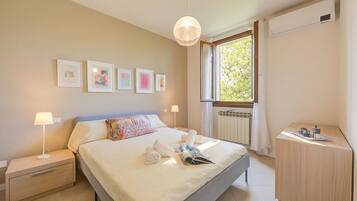 Habitación de hotel con cama, lámparas de noche, mesita de noche, ventana con vistas y obras de arte en la pared.