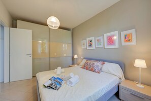 A hotel room with a bed, a nightstand, a lamp, a wardrobe, and wall art.