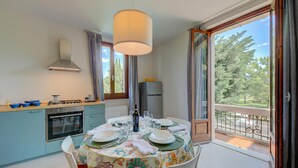 Un comedor con una mesa preparada para cuatro personas, una cocina con estufa y horno, y vistas a árboles desde un balcón.