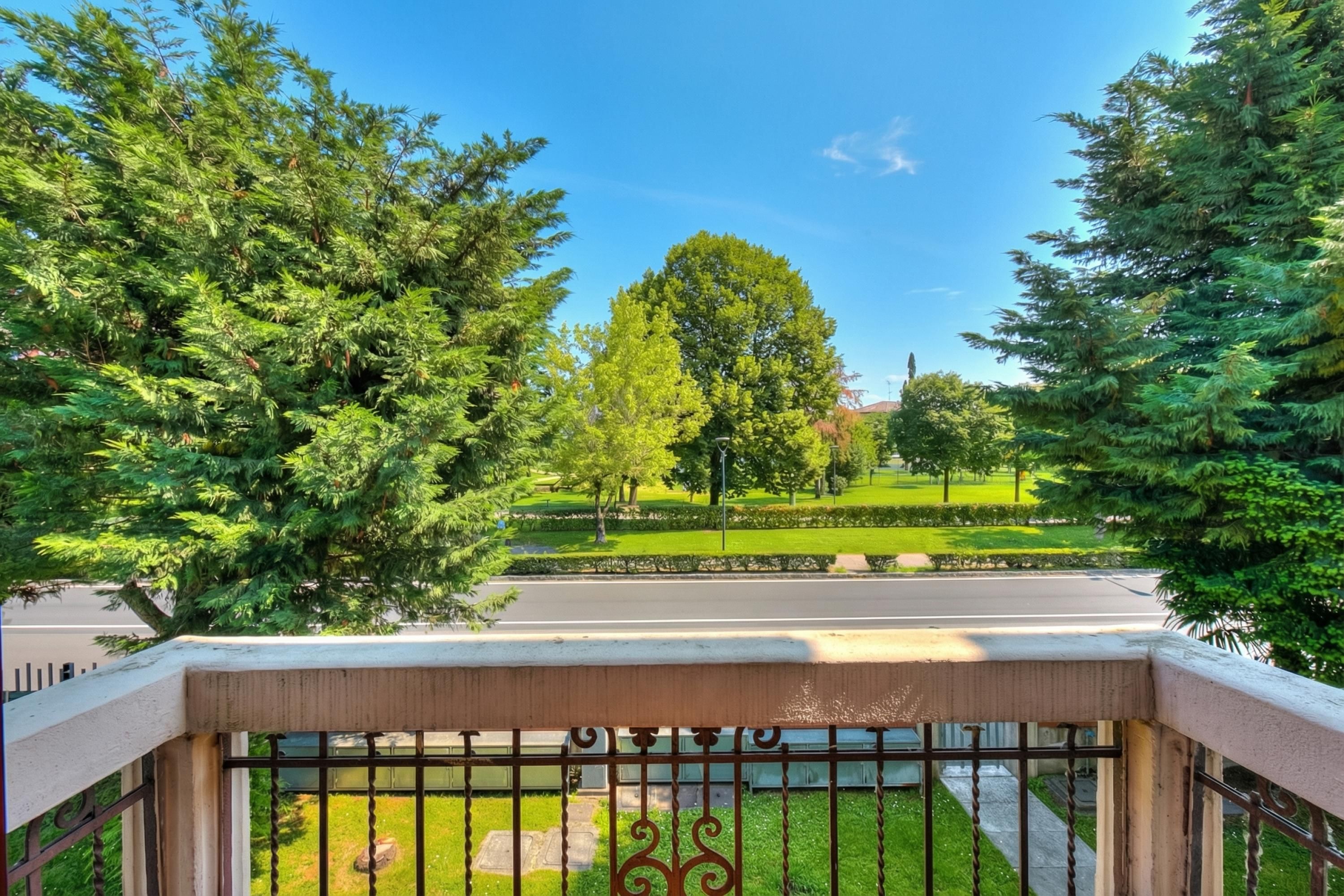 A balcony with a view of a park, a road, and a clear sky.