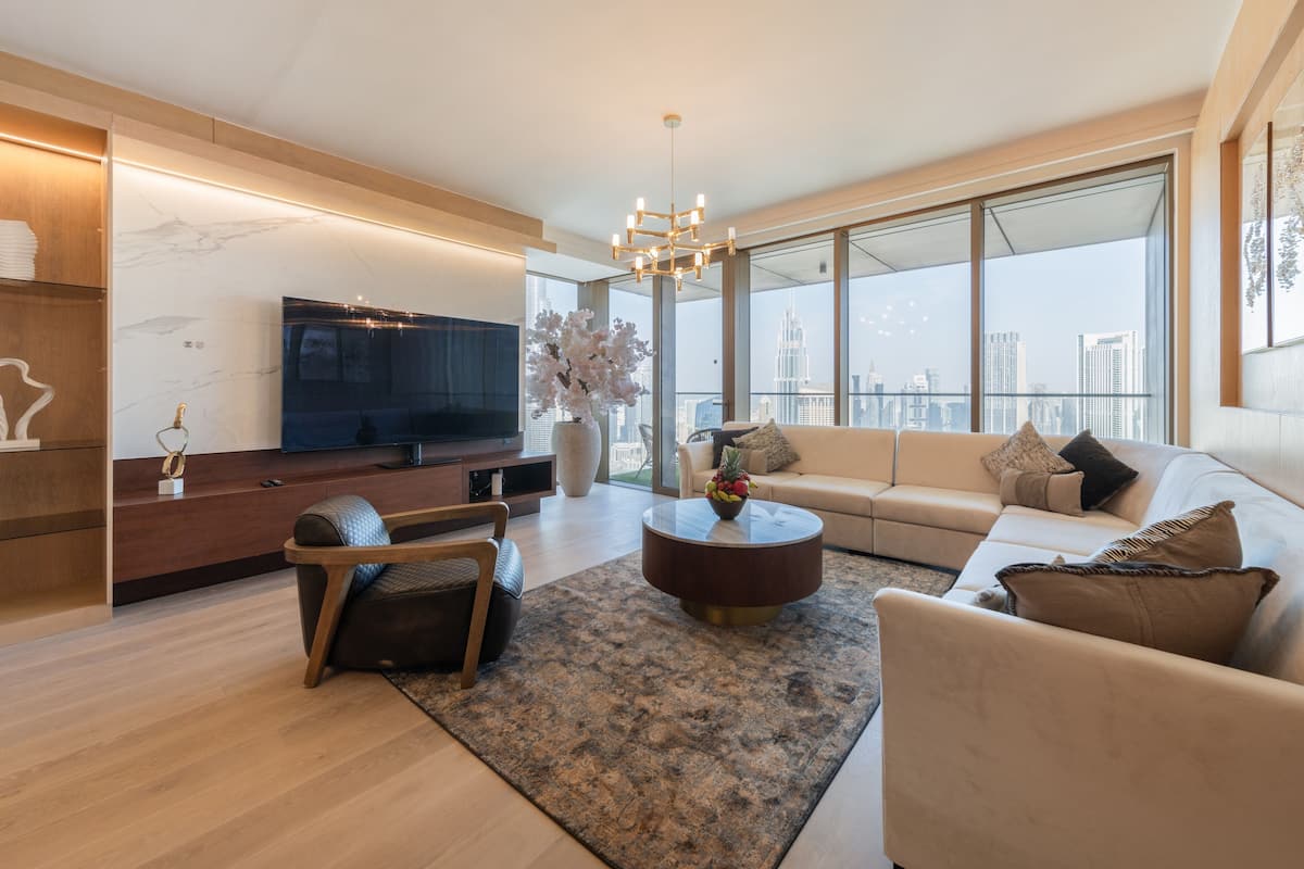 A modern living room with a large flat-screen TV, a sofa set, a coffee table, and a large window offering a city view.