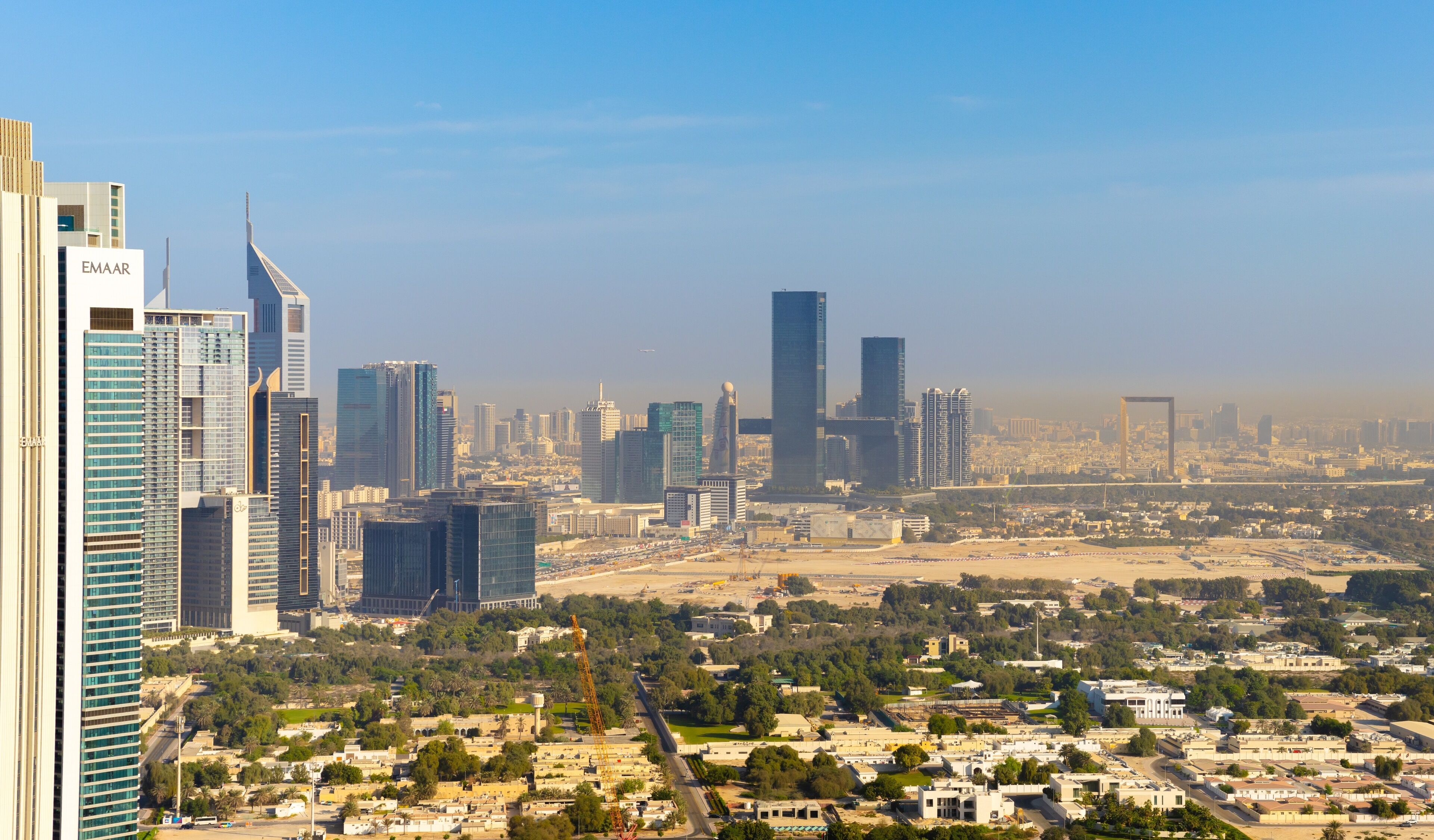 A cityscape with modern high-rise buildings, a clear sky, and a mix of urban and green areas.