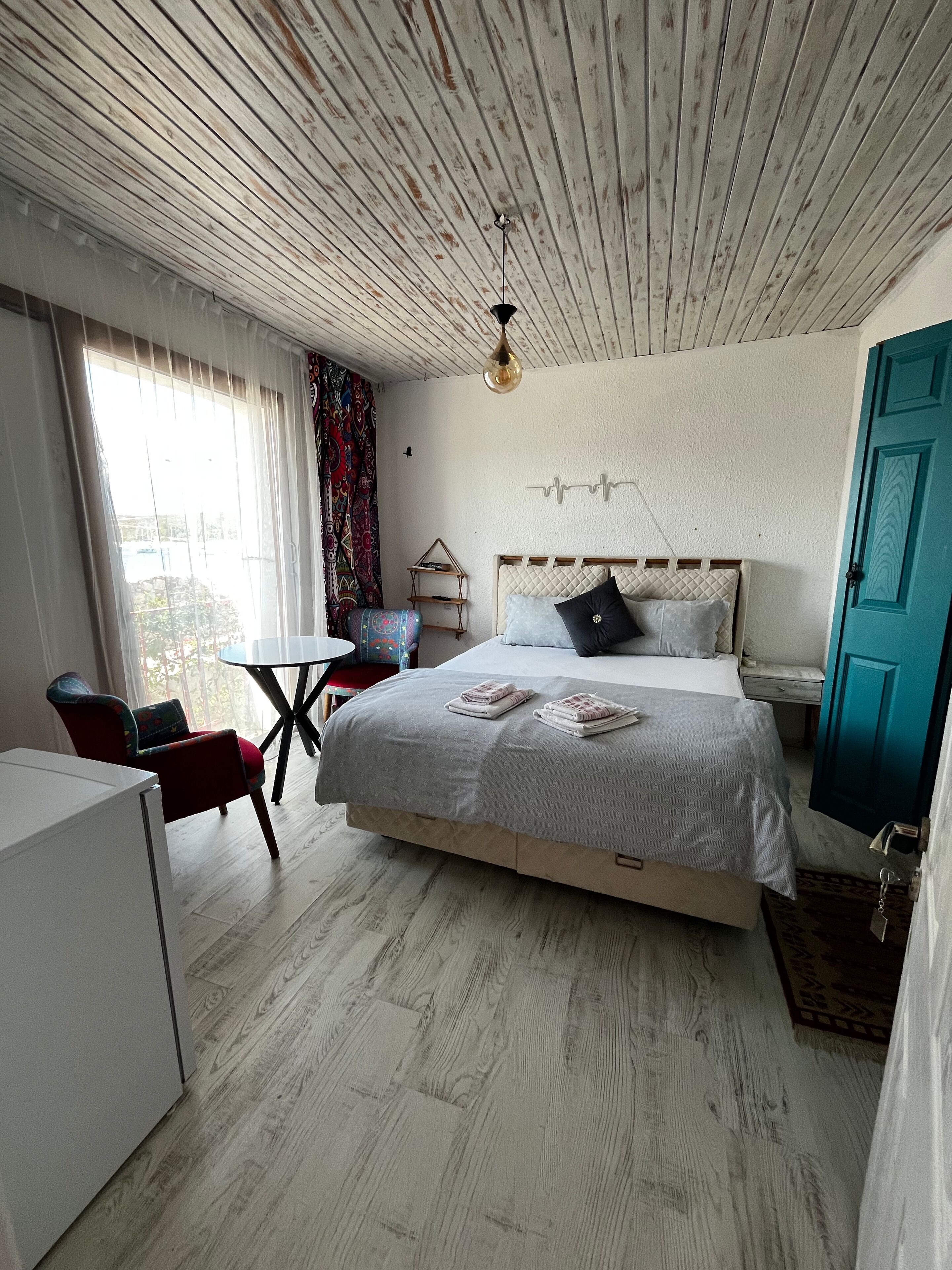 Une chambre à coucher avec un lit, un bureau, une chaise, une fenêtre avec des rideaux et une porte.