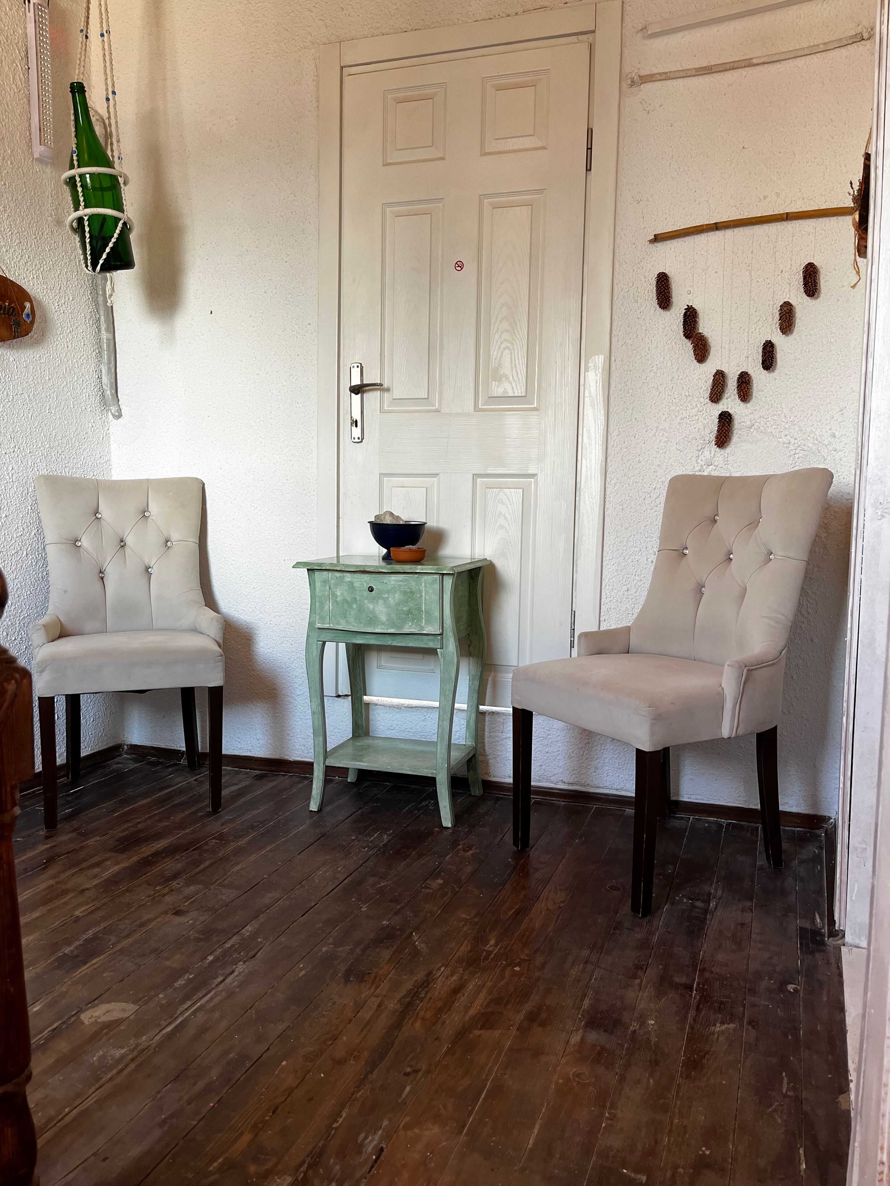 Une pièce comprenant deux fauteuils rembourrés, une petite table verte avec un bol, et une porte blanche portant une pancarte « accès interdit ».
