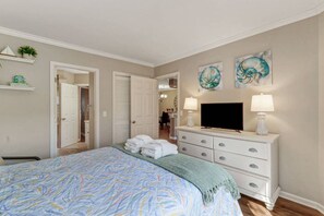 A bedroom with a bed, a TV, a dresser, and artwork on the wall.