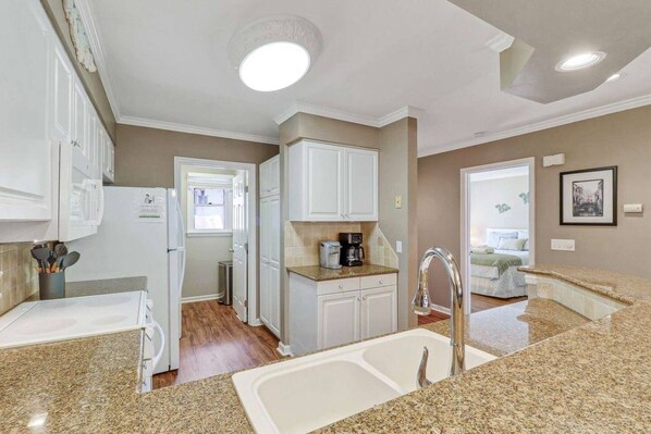 A modern kitchen with granite countertops, white cabinetry, a built-in oven, and a sink.