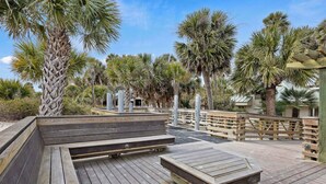 A wooden deck with benches and a wooden table, surrounded by palm trees and a wooden fence. - 145 Colonnade Club Villa Beach Path, Pool, Hot Tub (Hilton Head Island)